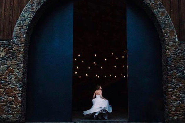 Young girl in a white dress sitting at the entrance of a dark, arched stone structure with star-like lights in the background.