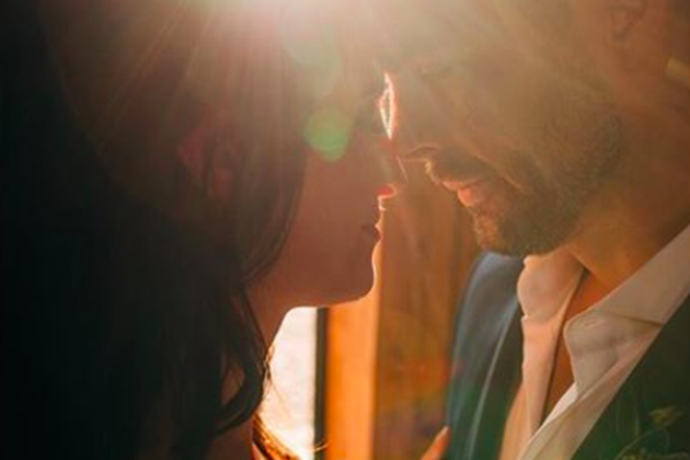 Close-up of a couple with their foreheads touching, backlit by warm sunlight, creating a romantic and intimate atmosphere.