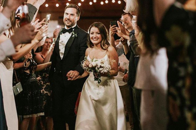 Bride and groom walking through guests at wedding reception, smiling and holding hands.