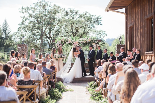 Outdoor wedding ceremony with bride and groom exchanging vows under floral arch.