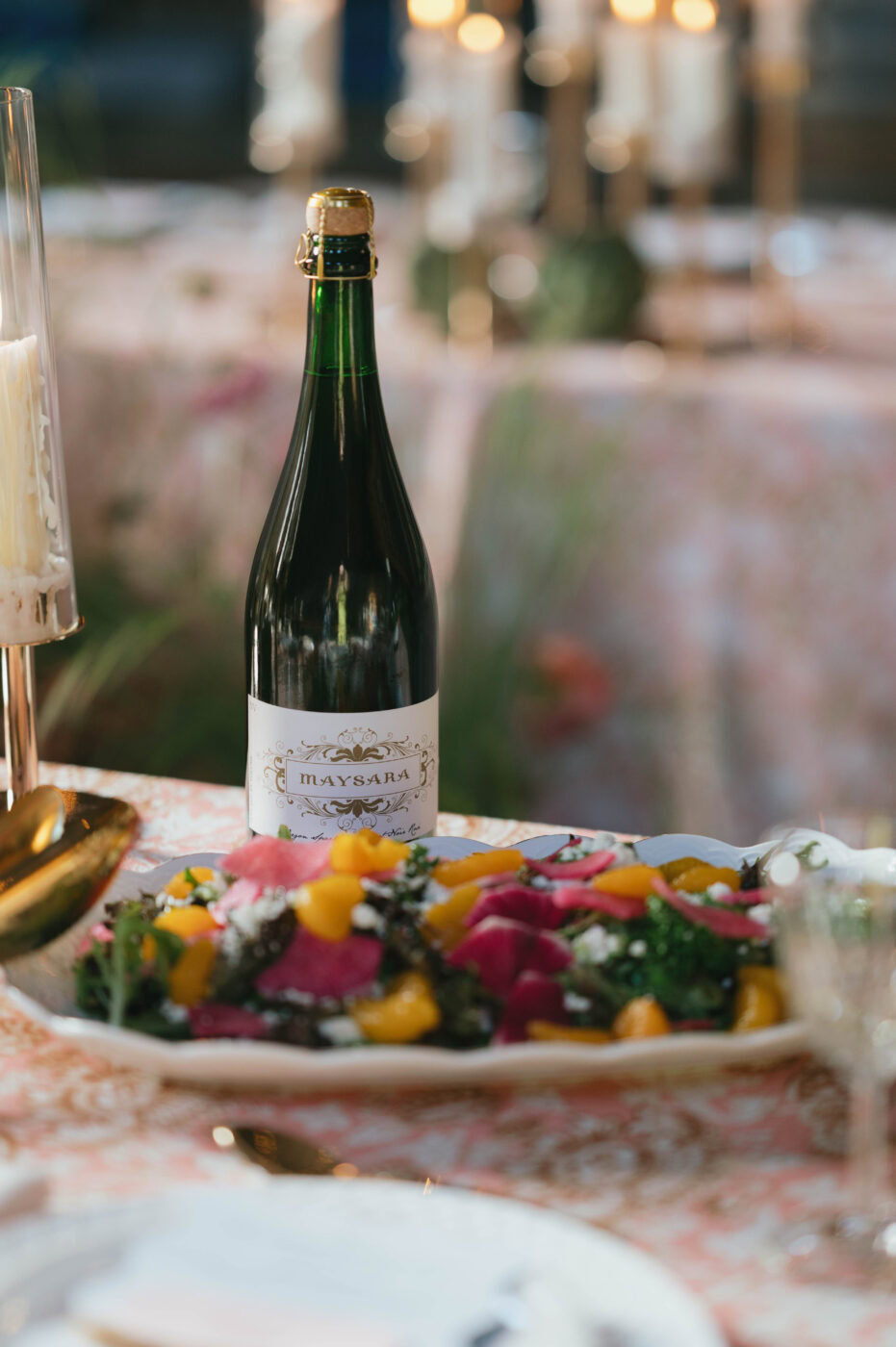Bottle of Maysara sparkling wine on a decorated table with colorful flowers and a blurred background.
